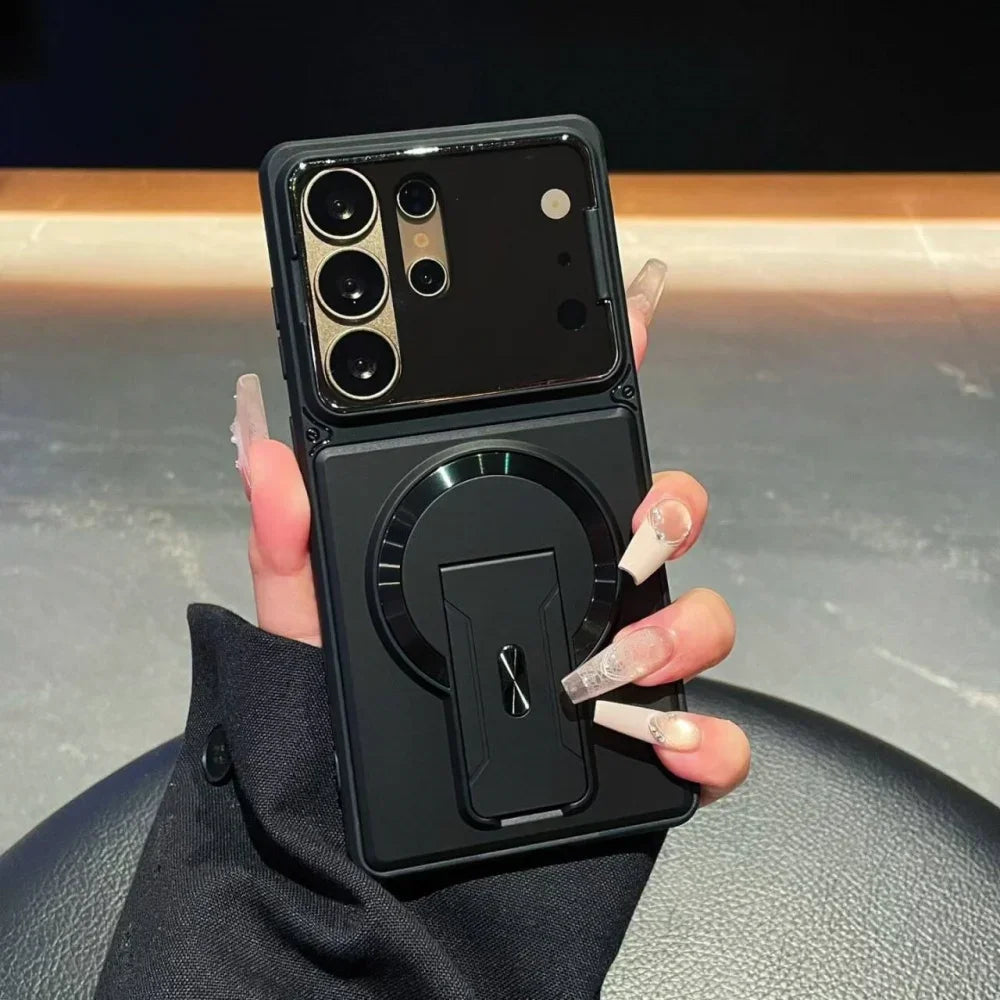 A black foldable phone case with an integrated circular kickstand and magnetic ring, held in a hand with long clear acrylic nails.