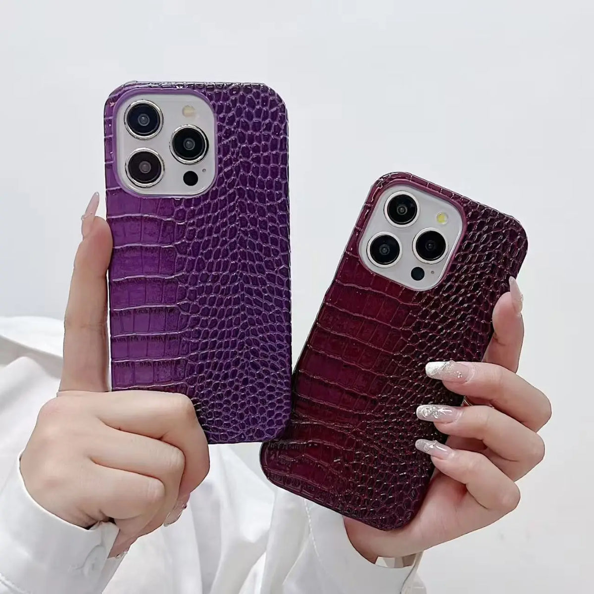 Two phone cases with purple and red crocodile texture held by a person against a white background