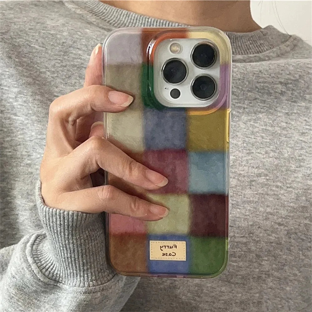 A person in a gray sweatshirt holds a phone with a colorful patchwork-patterned protective case. The case features a grid of various colored squares in shades of green, blue, yellow, pink, and purple, with a small beige label at the bottom that reads 'Case Party'.