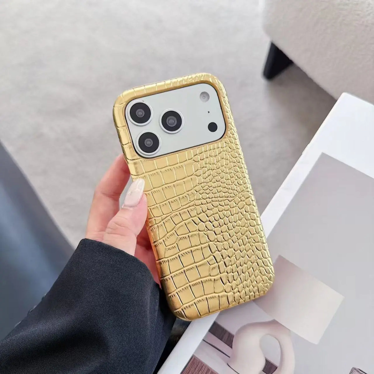 Gold crocodile-patterned phone case held by a hand on a light background