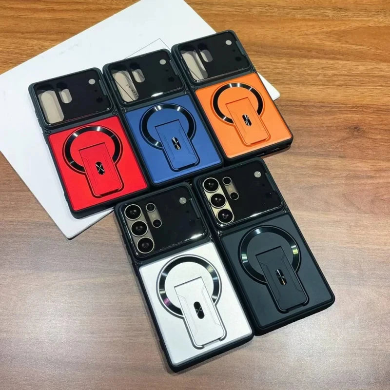 Six magnetic ring kickstand phone cases in different colors (black, red, blue, orange, silver, and dark gray) arranged on a wooden table next to a white box.