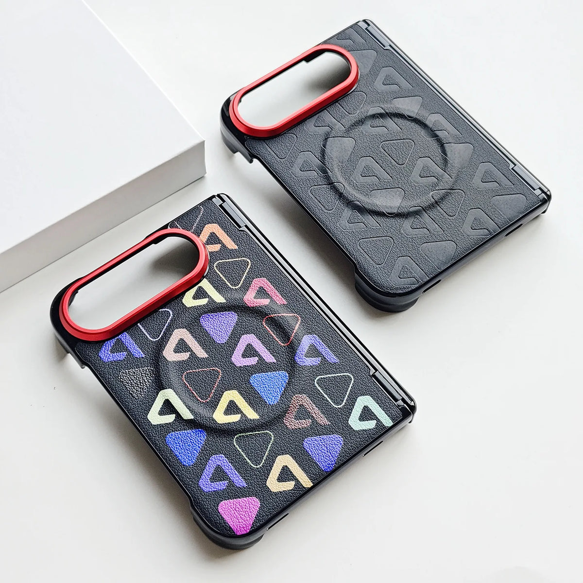 Two black protective phone cases with a geometric triangle pattern, one in solid colors and one in iridescent colors, both featuring a red raised camera ring and a built-in kickstand, displayed on a white surface.