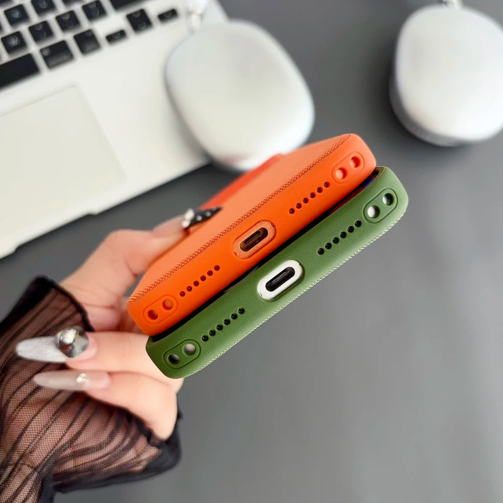 Two phone cases, one orange and one green, held by a hand with a blurred office background.