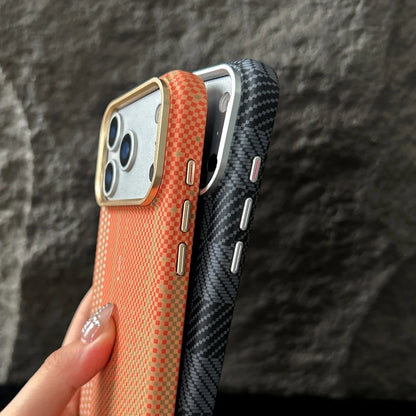 Two phone cases, one orange and one black carbon fiber pattern, held against a dark stone wall.