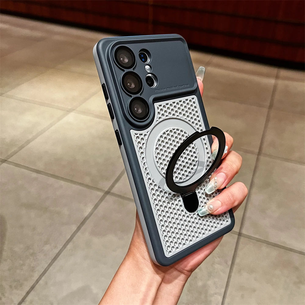 A hand holding a dark gray and silver phone case with a built-in black ring stand, shown against a tiled indoor floor background.