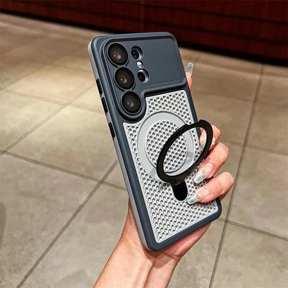A hand holding a dark gray and silver phone case with a built-in black ring stand, shown against a tiled indoor floor background.