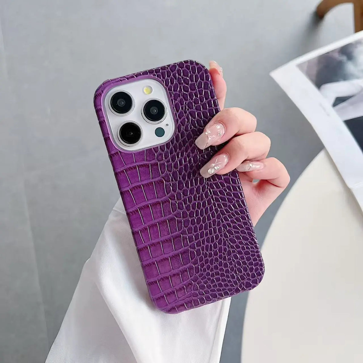 Purple crocodile texture phone case held by a hand on a gray background