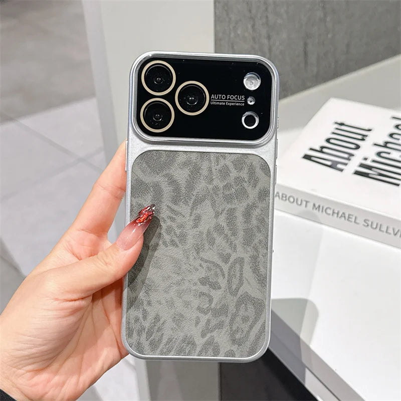 A hand holds a smartphone case with a gray textured back panel and a black camera cutout area, shown in an indoor setting with a book in the background.