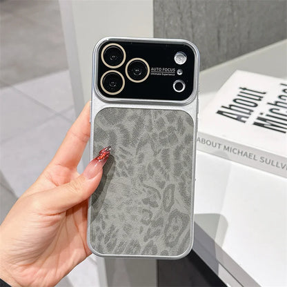 A hand holds a smartphone case with a gray textured back panel and a black camera cutout area, shown in an indoor setting with a book in the background.