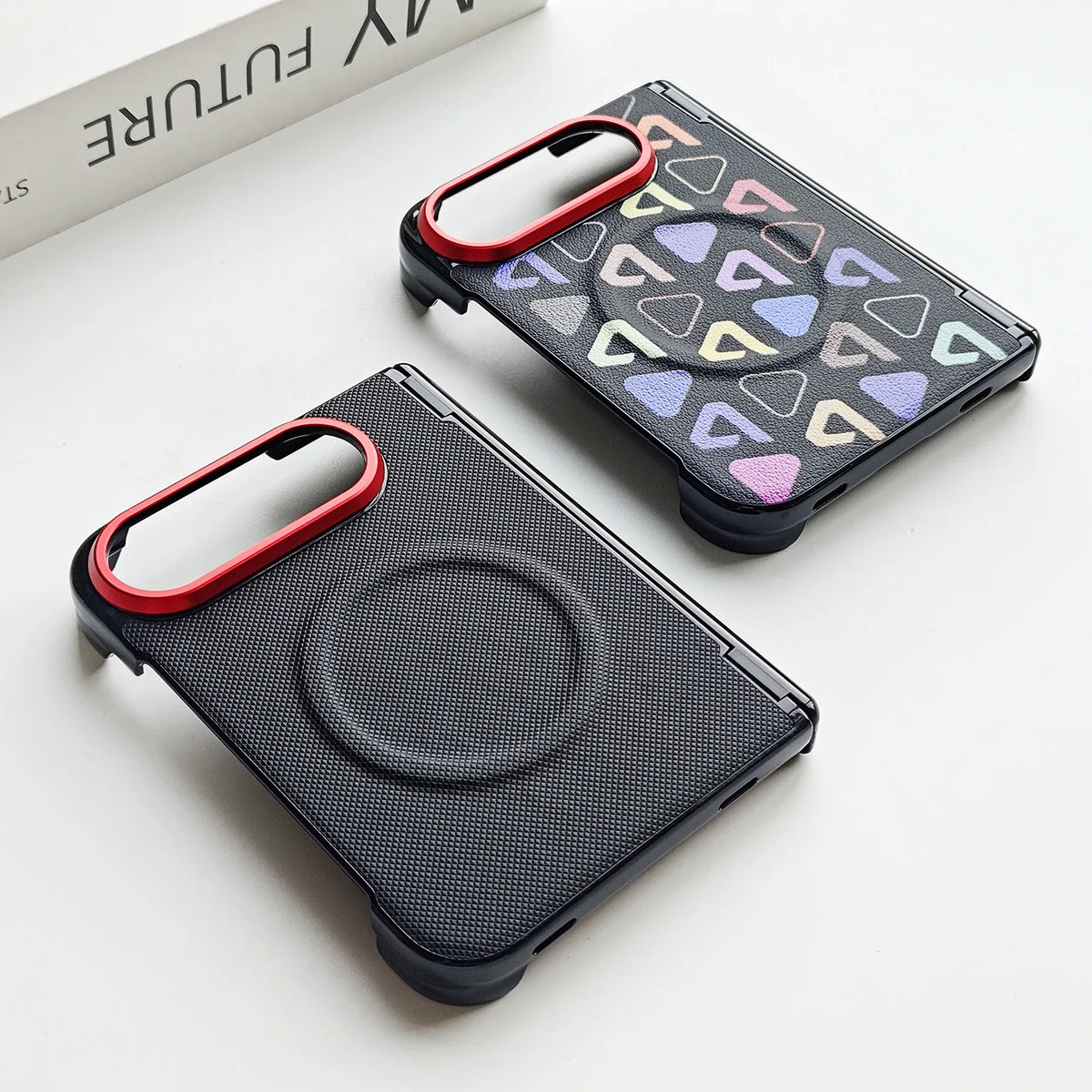 Two black textured phone cases with circular magnetic rings and camera cutouts, shown on a white surface. One case has a red camera ring accent, and the other has a pattern of pastel geometric triangles.