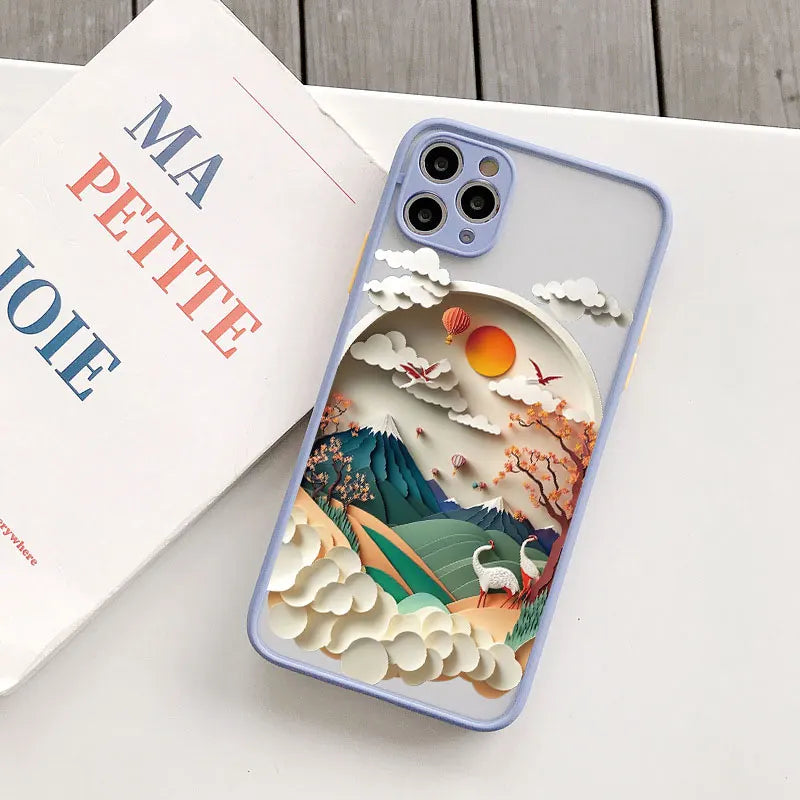 Phone case with a mountain and cloud design on a white surface with a coffee cup and book.