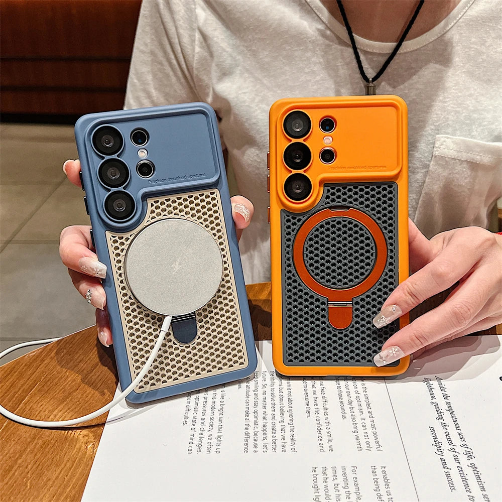 Two phone cases with a textured honeycomb design and a circular MagSafe ring are held by a person over a wooden table. One case is slate blue and the other is orange, both fitted on dark gray phones.