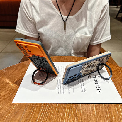 Two smartphone cases displayed on a wooden table, each holding a phone and featuring a circular ring stand. One case is orange and dark gray, and the other is light blue and beige.